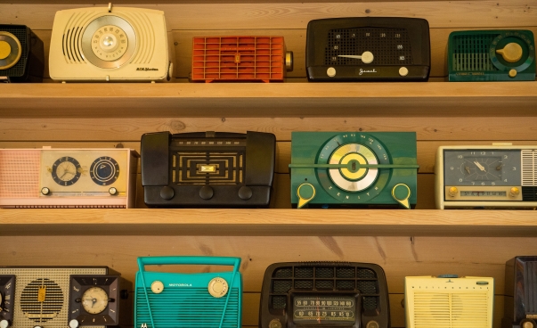 Mehrere alte, bunte Radios stehen in einem Regal nebeneinander.